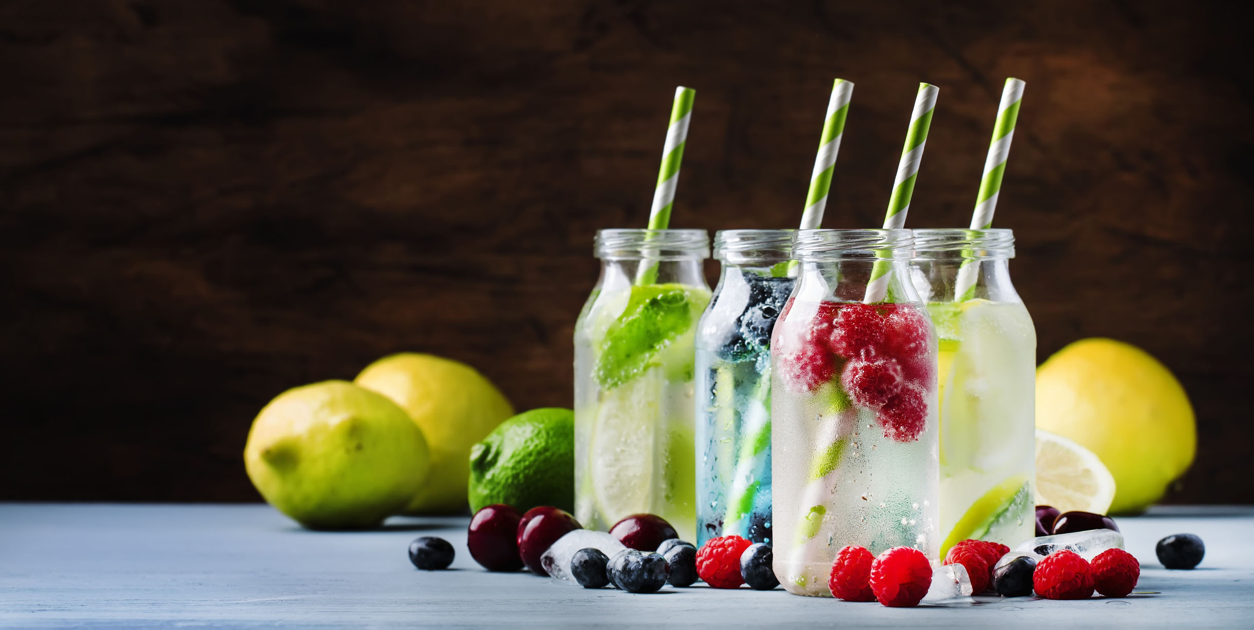 Summer drinks set. Berry, fruit and citrus non-alcoholic refreshing ice cold beverages and cocktails in glass bottles on blue background